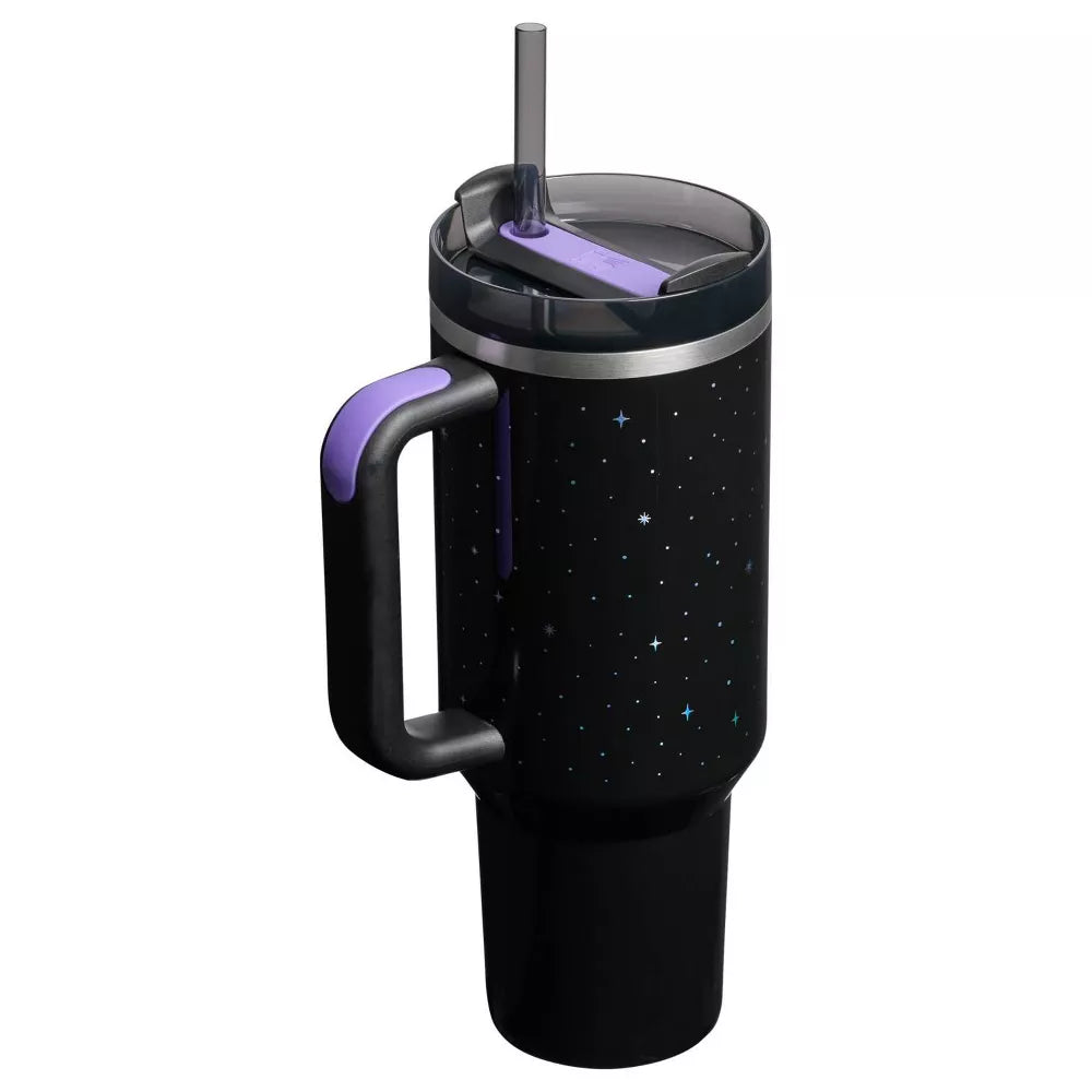 Close-up of the lid and handle of the Stanley Quencher Halloween tumbler. The dark gray lid has a purple FlowState™ flip closure, and the black body features a custom glow-in-the-dark (or iridescent) star and bat graphic, with the Stanley logo.